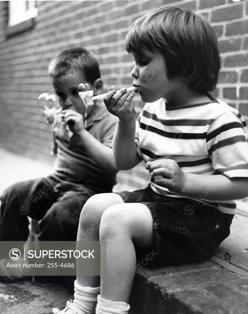 Two boys sitting on curb blowing bubbles