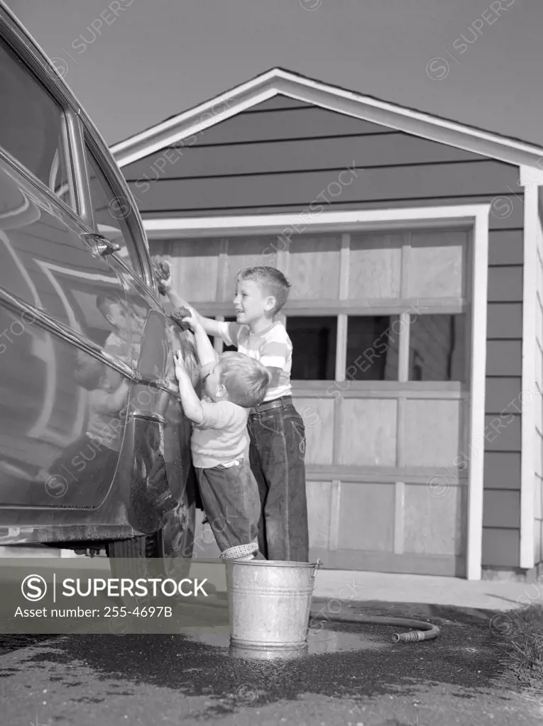 Two boys cleaning car in front of house