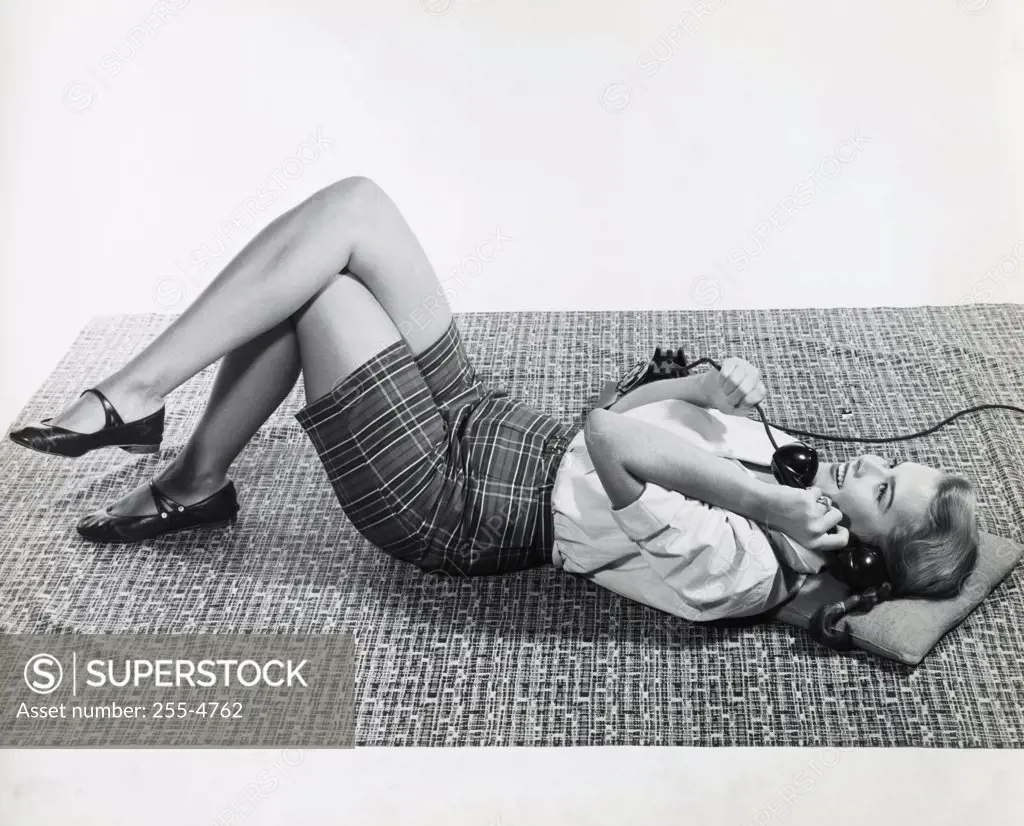 Side profile of a teenage girl lying on her back and talking on the phone, 1958