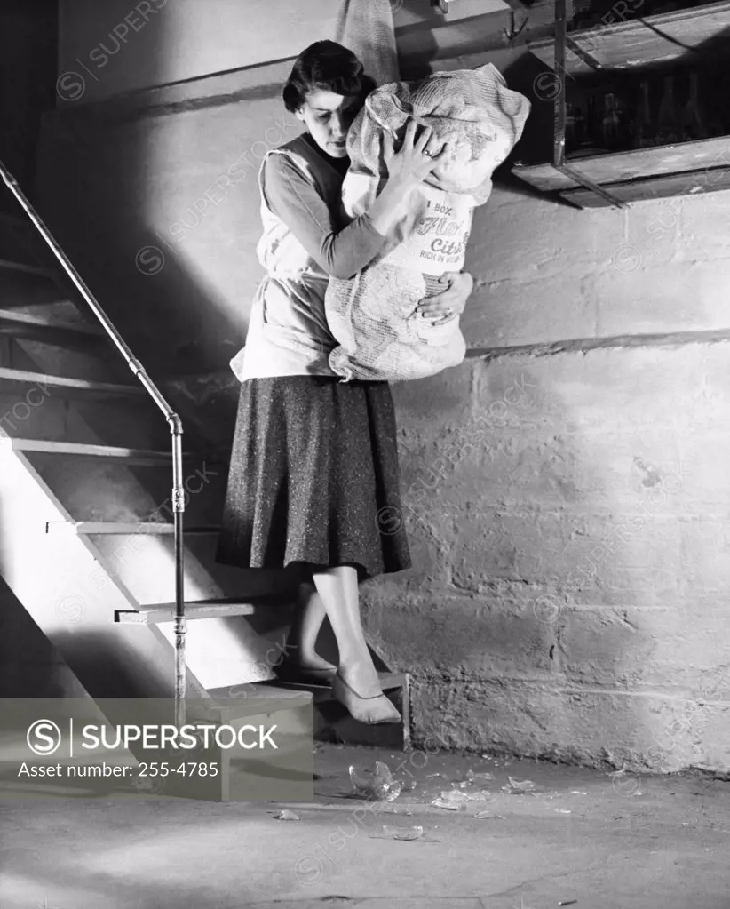 Mid adult woman moving down a staircase with a sack