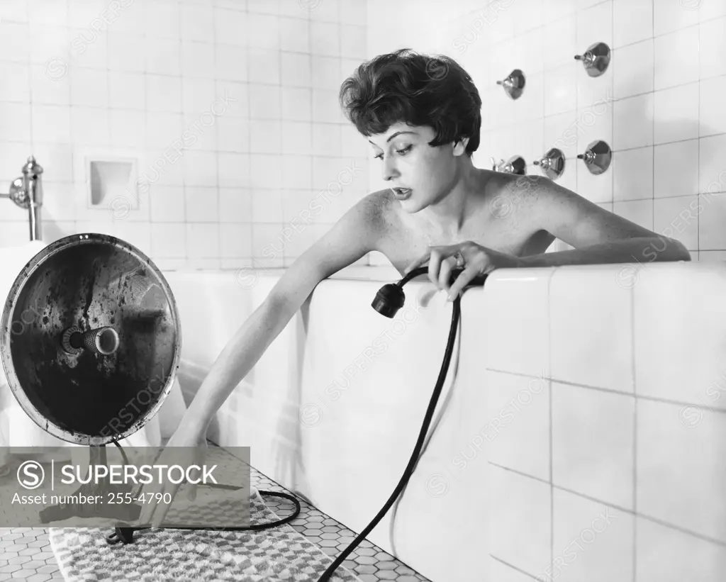 Young woman in a bathtub and holding a radiator's cable