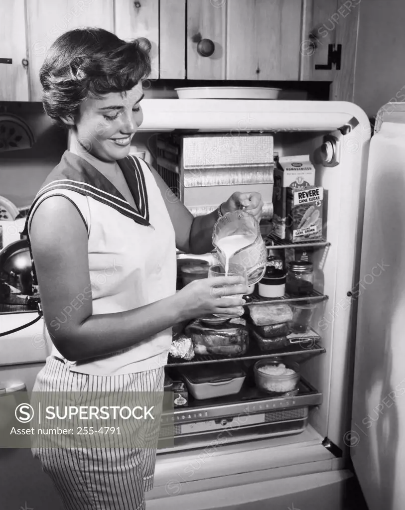 Side profile of a young woman standing near a refrigerator pouring milk