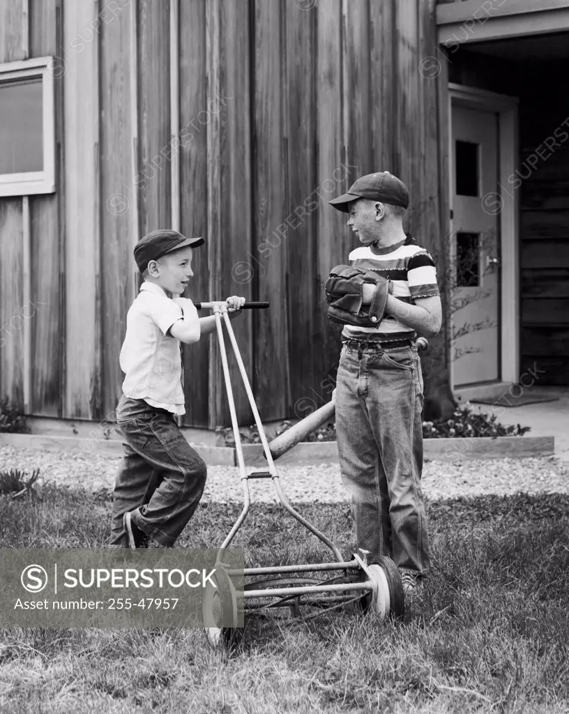 Boy mowing the lawn with a lawn mower and his friend talking to him