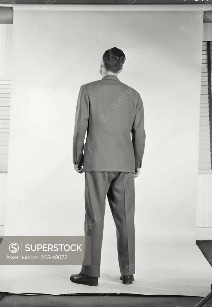 Vintage Photograph. Full length portrait back view of man in suit and tie standing on solid background