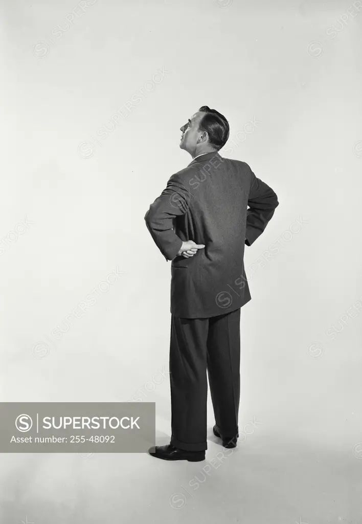 Vintage Photograph. Man in suit and tie standing on white background with hands behind back.