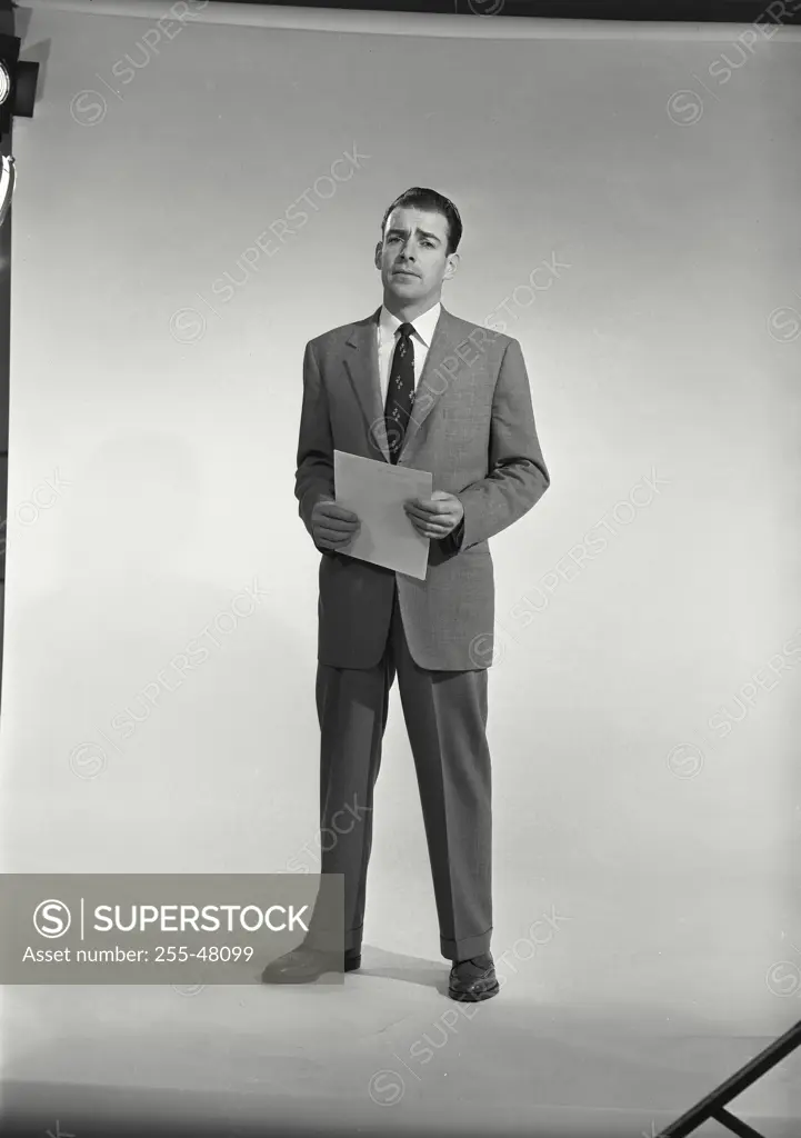 Vintage Photograph. Man in suit and tie holding sheet of paper on white background. Frame 1