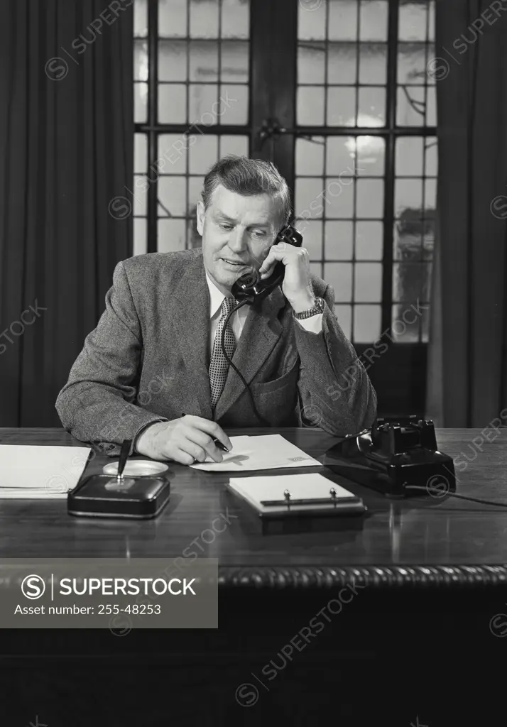 Vintage Photograph. Man in suit sitting at desk talking on telephone. Frame 1