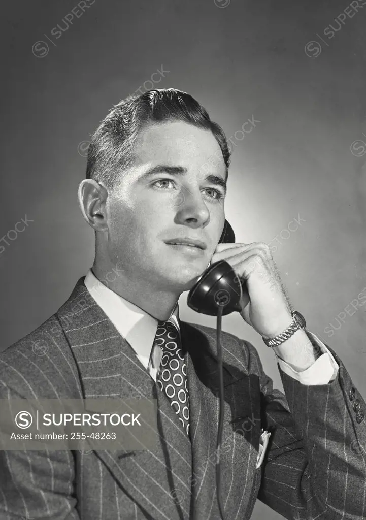 Young businessman wearing pinstriped suit and tie holding telephone receiver to ear