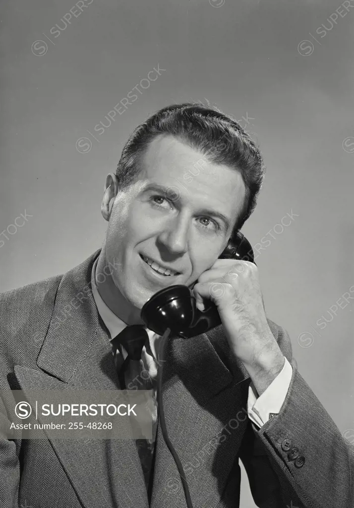 Vintage Photograph. Dark haired man in suit smiling while talking on the phone