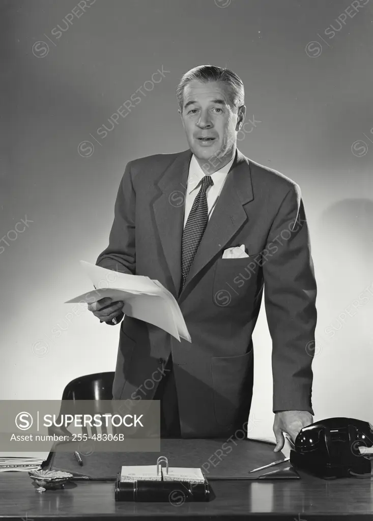 Vintage Photograph. Man in suit standing with stack of papers in hand