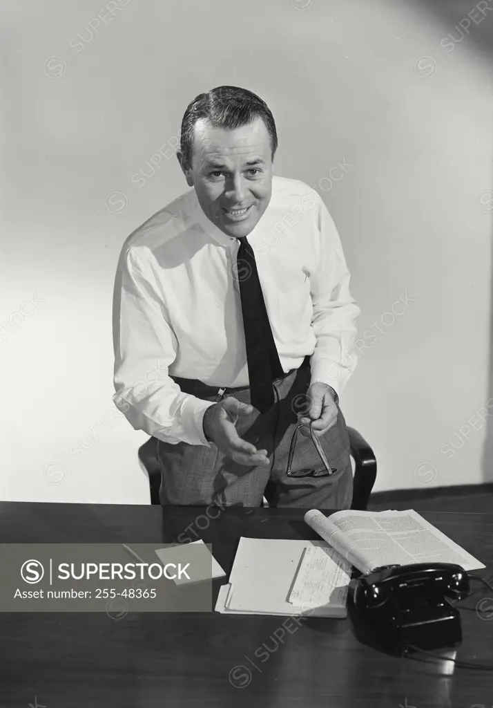 Vintage Photograph. Man wearing dress shirt holding eyeglasses standing at desk with hand outstretched for handshake, Frame 2