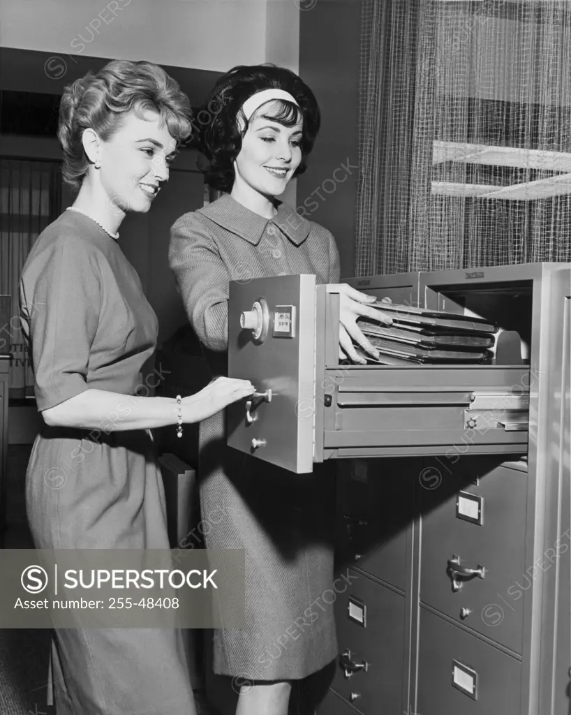 Two female office workers arranging files in filing cabinet