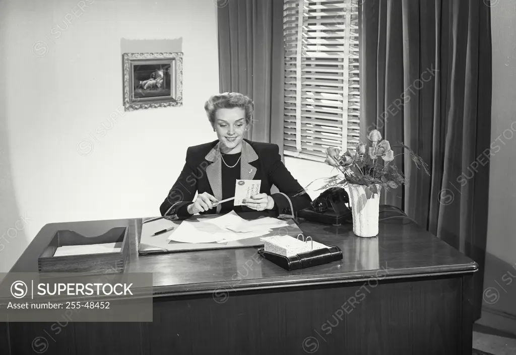 Vintage Photograph. Woman sitting at desk opening letters with letter opener