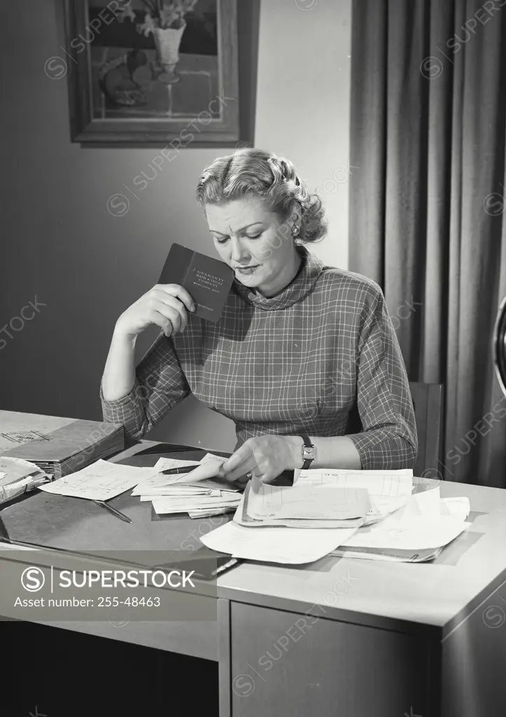 Vintage Photograph. Woman in longsleeve blouse balancing checkbook at desk