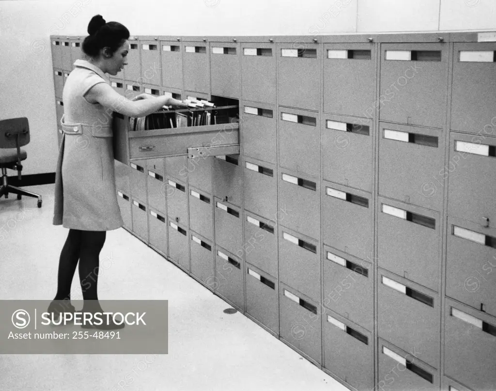 Side profile of a businesswoman searching for files in a filing cabinet
