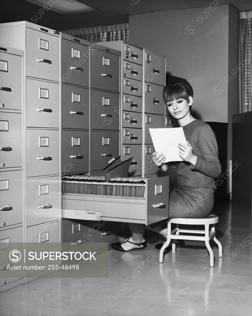 Businesswoman reading a document beside a filing cabinet