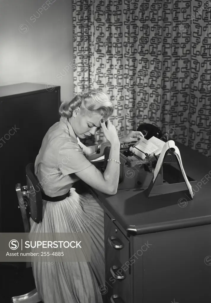 Vintage Photograph. Smiling young woman sitting at office desk with typewriter holding head in discomfort