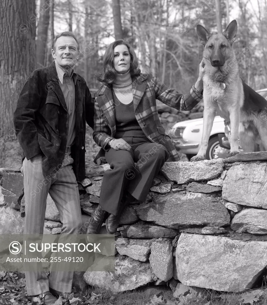 Portrait of mature couple with dog sitting on stone wall