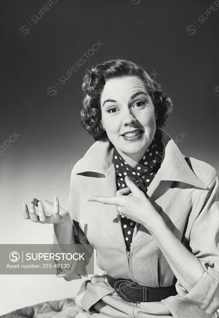 Vintage Photograph. Woman with curly hair wearing coat with wide collar over polka dot blouse pointing to empty hand