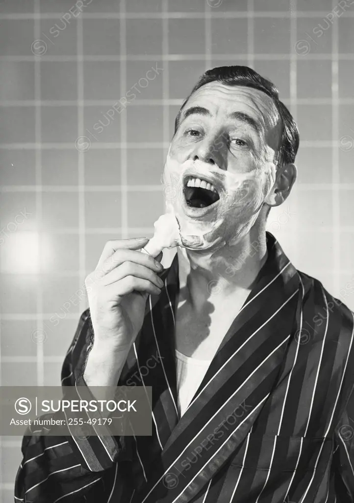 Vintage photograph. Portrait of a mid adult man in robe applying shaving cream