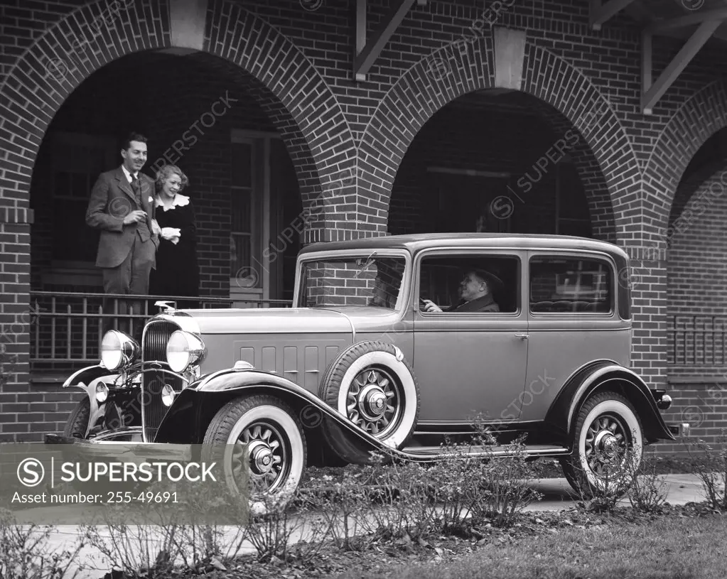 Couple looking at a 1932 Oldsmobile parked in front of a house