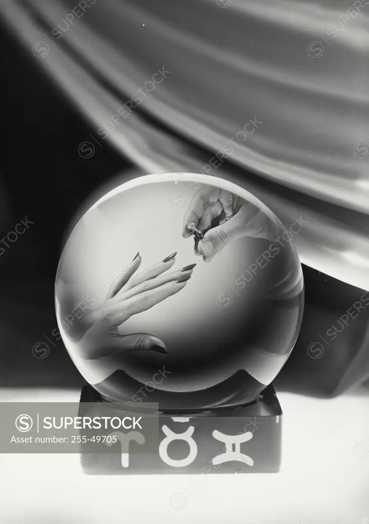Vintage Photograph. Crystal ball showing male hand placing ring on female finger in center with fabric draped behind and symbols on base