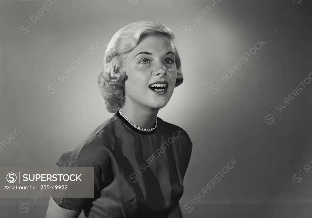 Vintage Photograph. Smiling young woman with short blonde hair wearing high collared blouse with mouth open looking up and off camera
