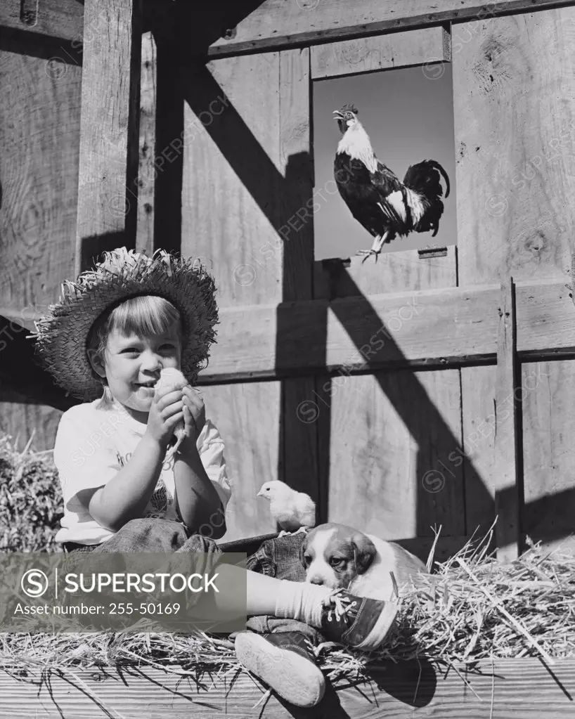Girl sitting on a heap of hay and holding a chick