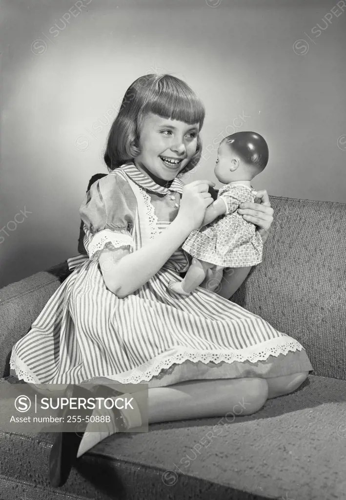 Vintage photograph. Portrait of young girl in dress sitting smiling with doll