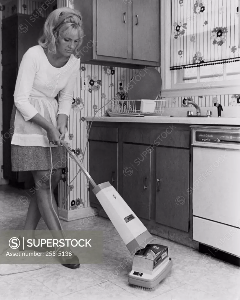 Young woman using vacuum cleaner in kitchen