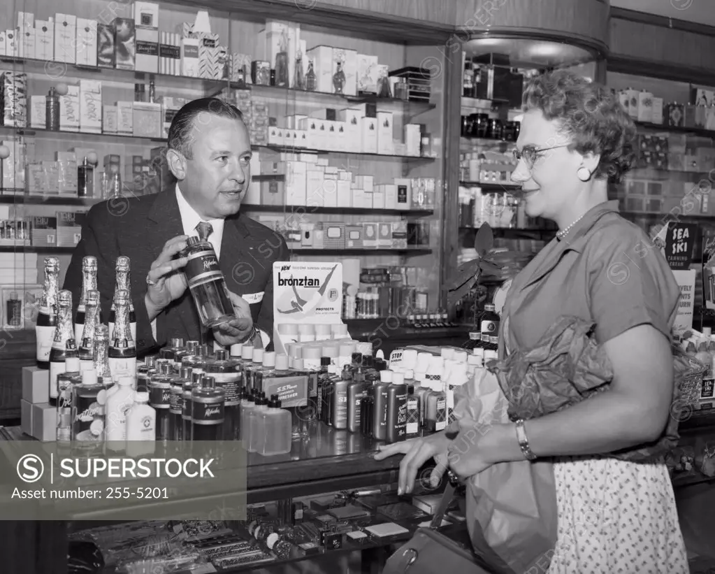Salesman showing bottle to mid adult woman in store