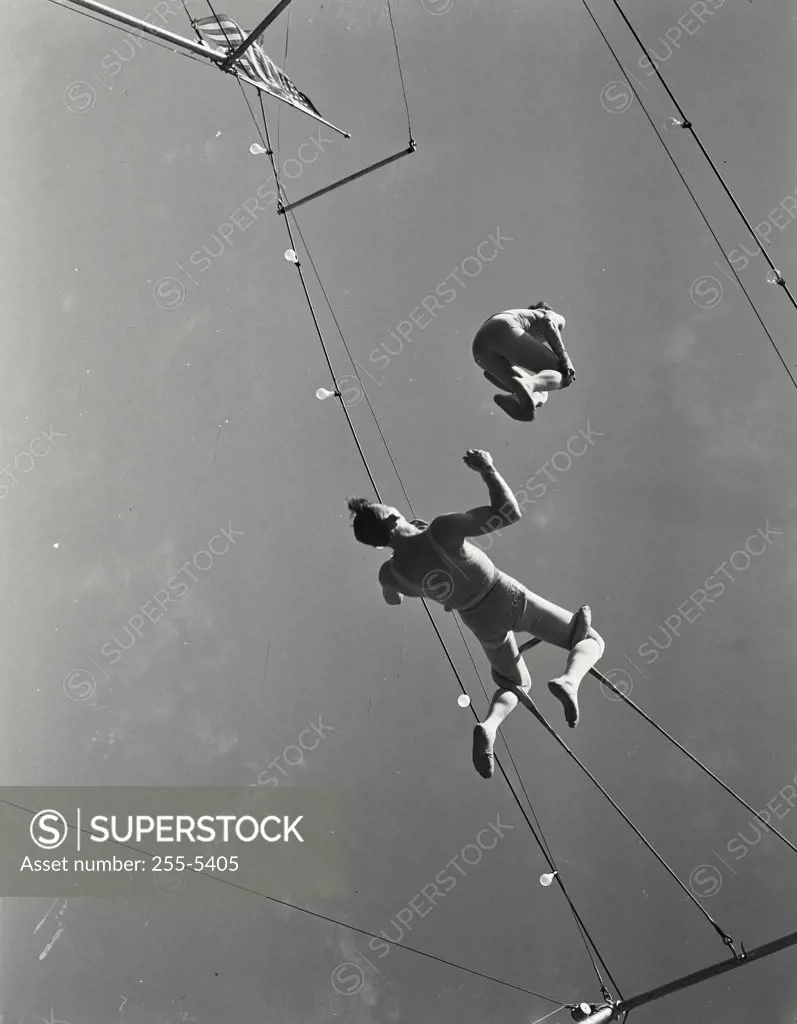Vintage photograph. Low angle view of trapeze artists performing in a circus