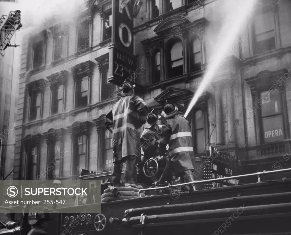 Low angle view of three firemen spraying water on a burning movie theater, New York City, New York State, USA