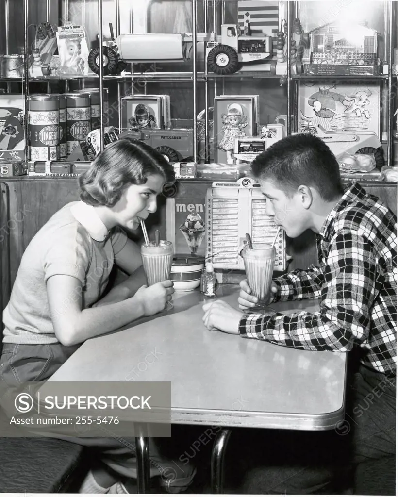 Side profile of a young couple drinking a milkshake in a restaurant, 1954