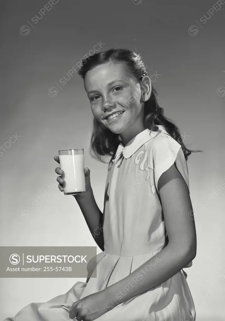 Vintage Photograph. Smiling girl in white diress holding up glass of milk