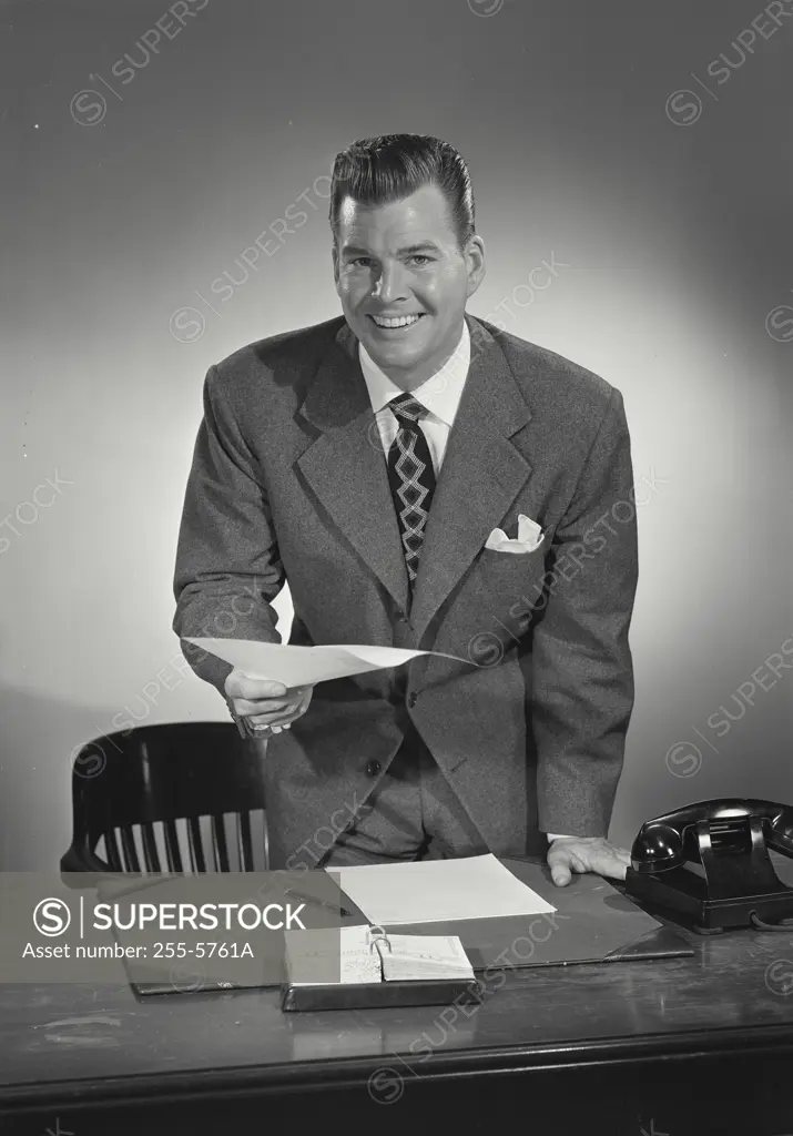 Smiling businessman standing behind desk with document in hand