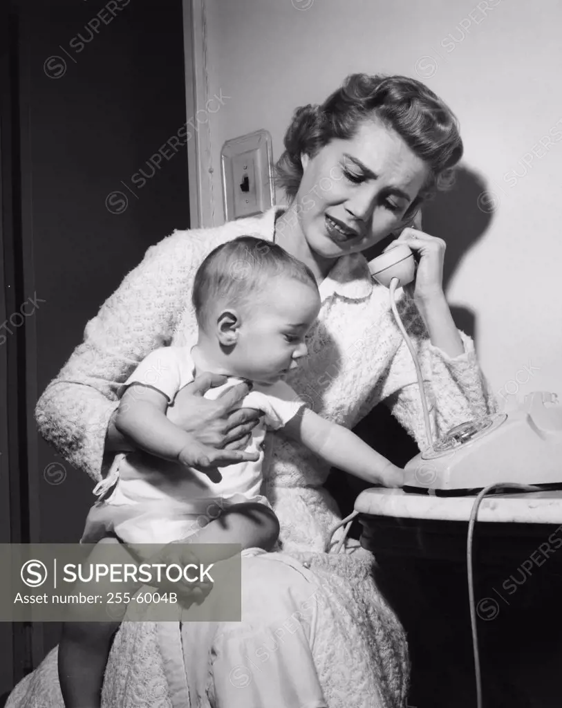 Mother with baby boy on laps talking on phone