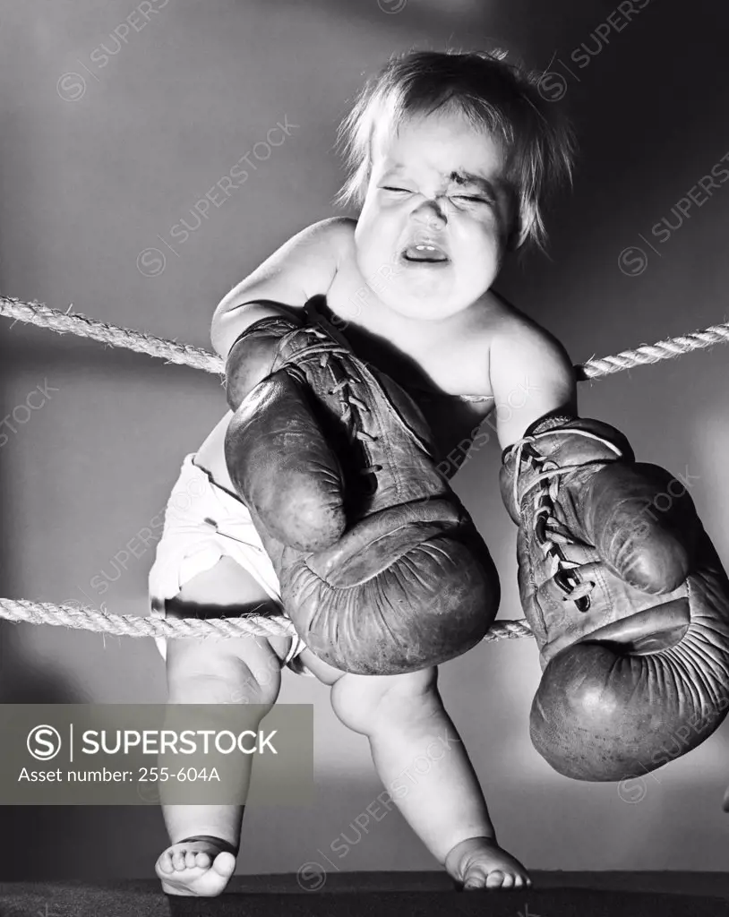 Close-up of a crying baby wearing boxing gloves