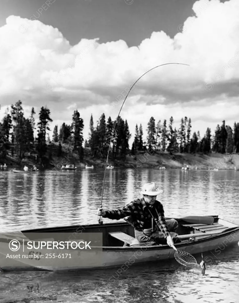 Mid adult man sitting on a rowboat and fishing in a lake