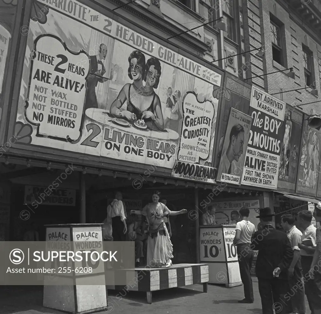 Vintage photograph. Woman and band on small stage under large sign for a side show advertising 2 headed girl and boy with two mouths