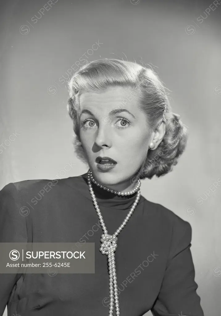 Vintage Photograph. Blonde woman wearing pearl necklace wrapped in knot with surprised look on face