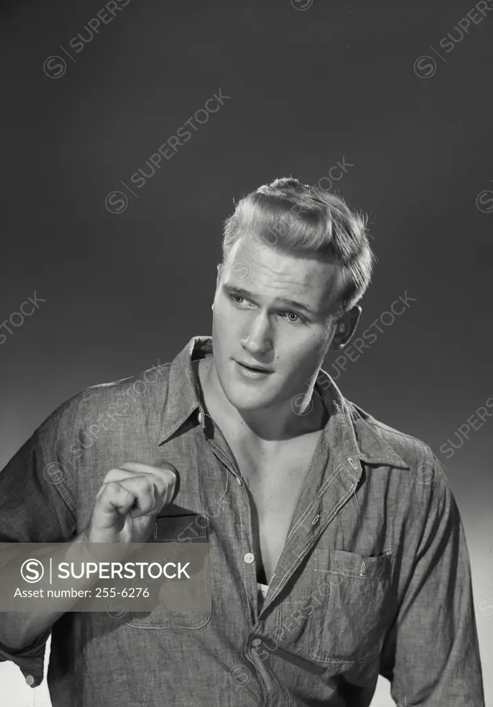 Vintage Photograph. Blonde man wearing chambray work shirt holding up hand pointing thumb back at chest