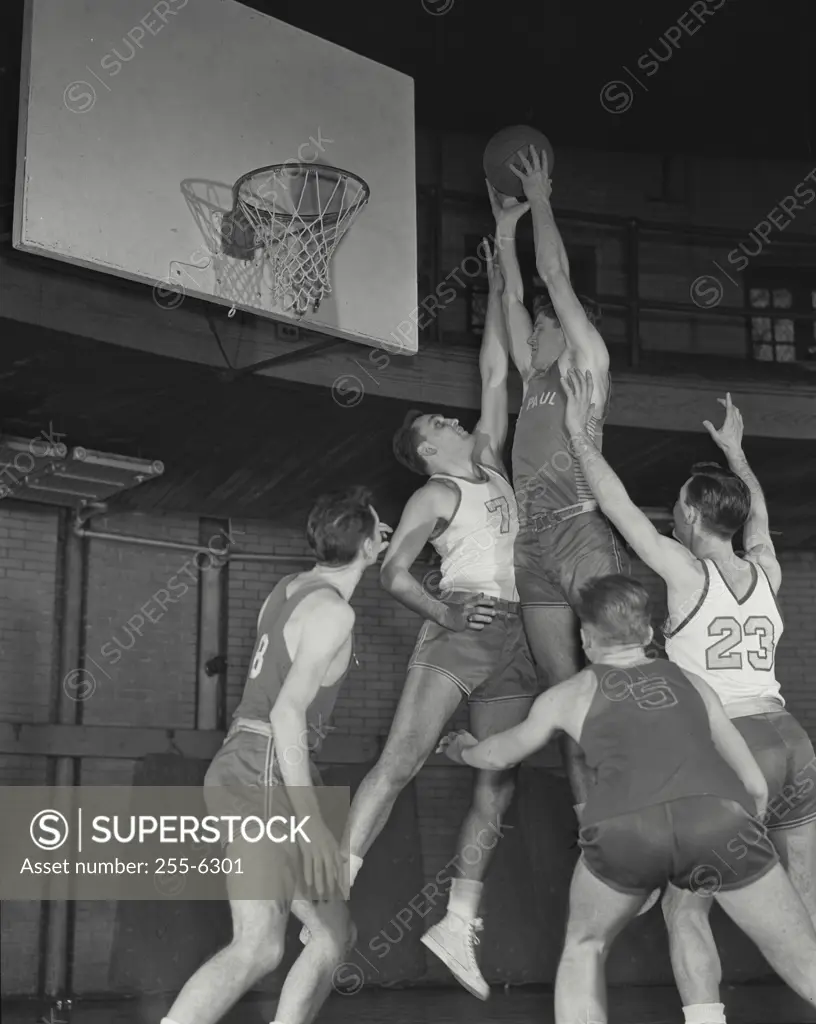 Vintage Photograph. Basketball player jumping high over defenders to shoot ball at basket