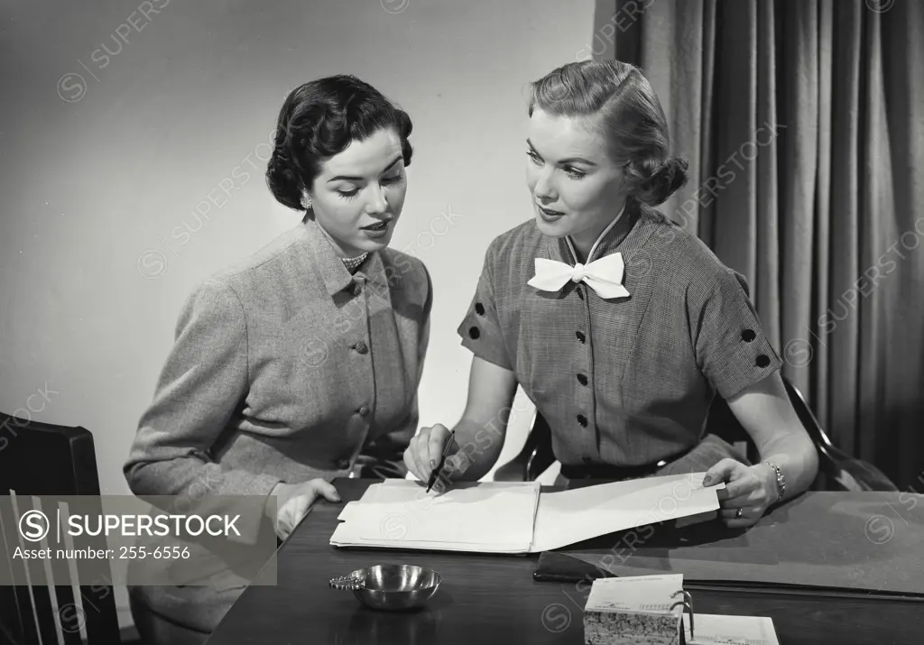 Vintage Photograph. Two women in business office sitting at desk having conversation, woman on right pointing out line on document