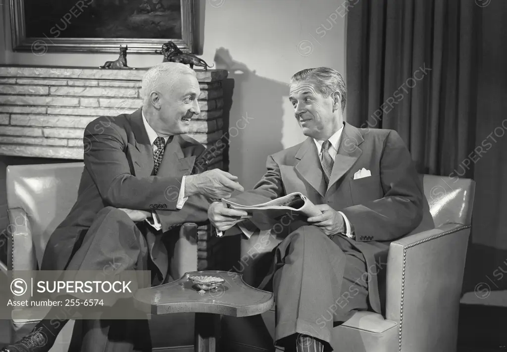 Vintage Photograph. Men in suits sitting in chairs talking with each other over newspaper