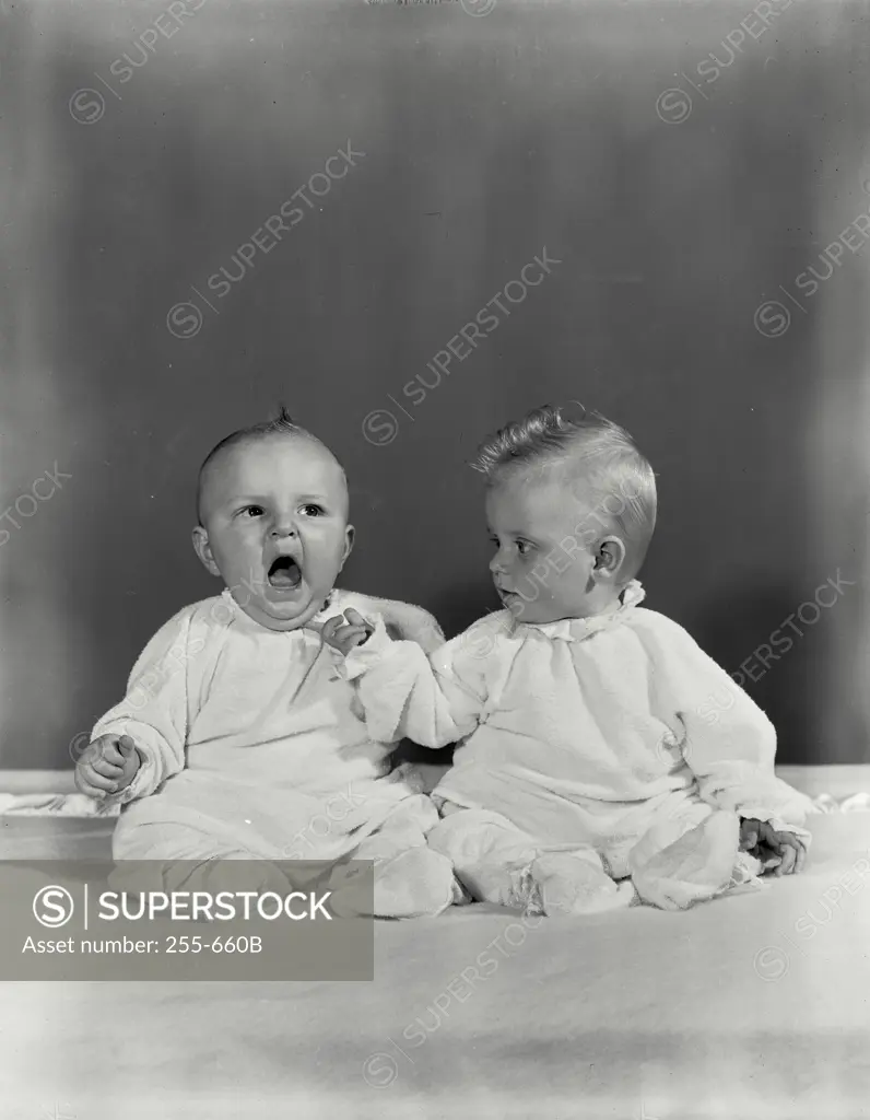Vintage Photograph. Two babies on blanket, one yawning, the other touching chin of the first