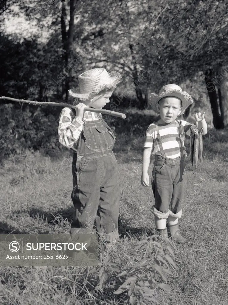 Two boys with bunch of fish and fishing rod made of stick in field