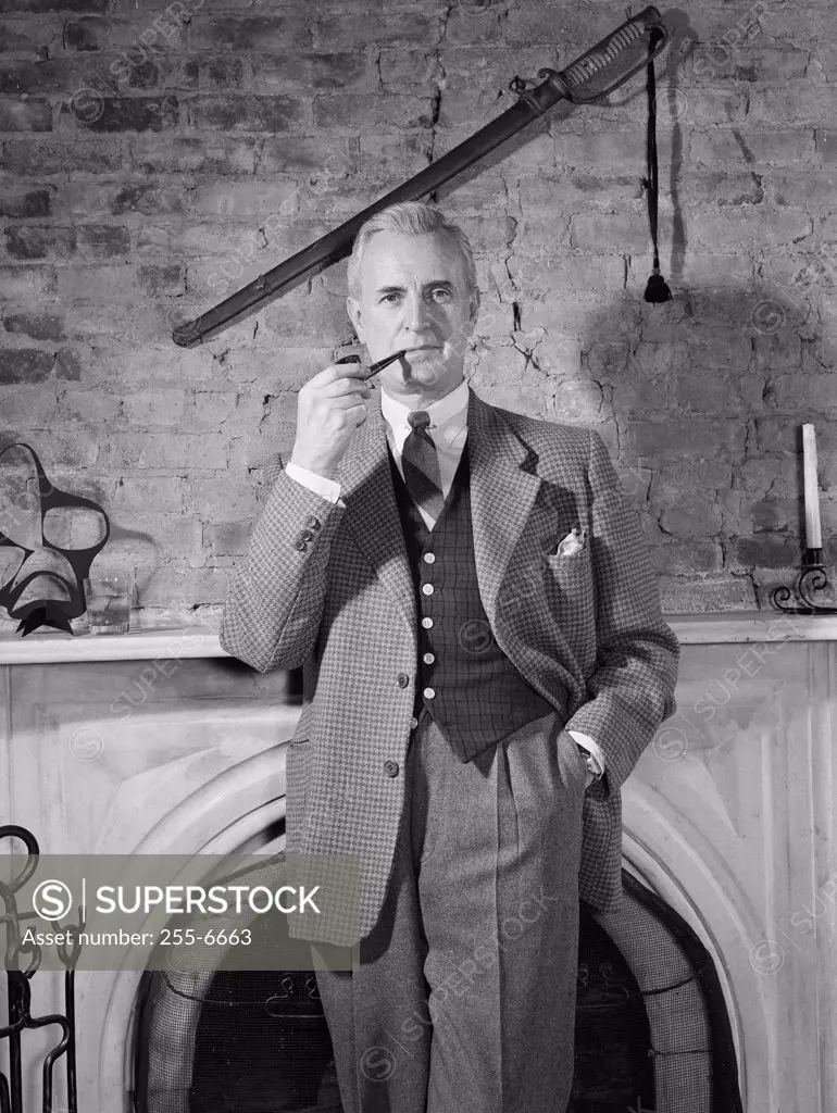 Elegant man standing by fireplace and smoking pipe