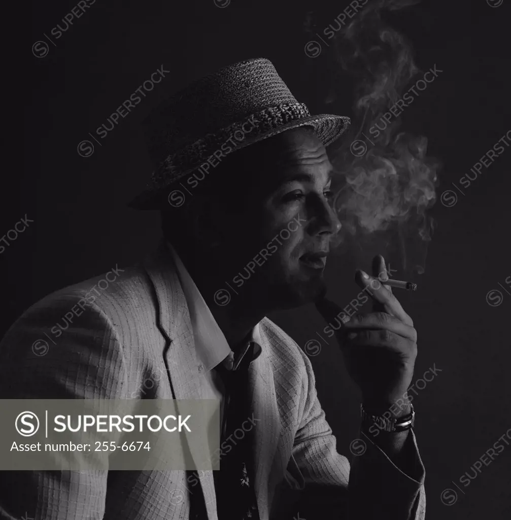 Studio portrait of man wearing hat, smoking cigarette
