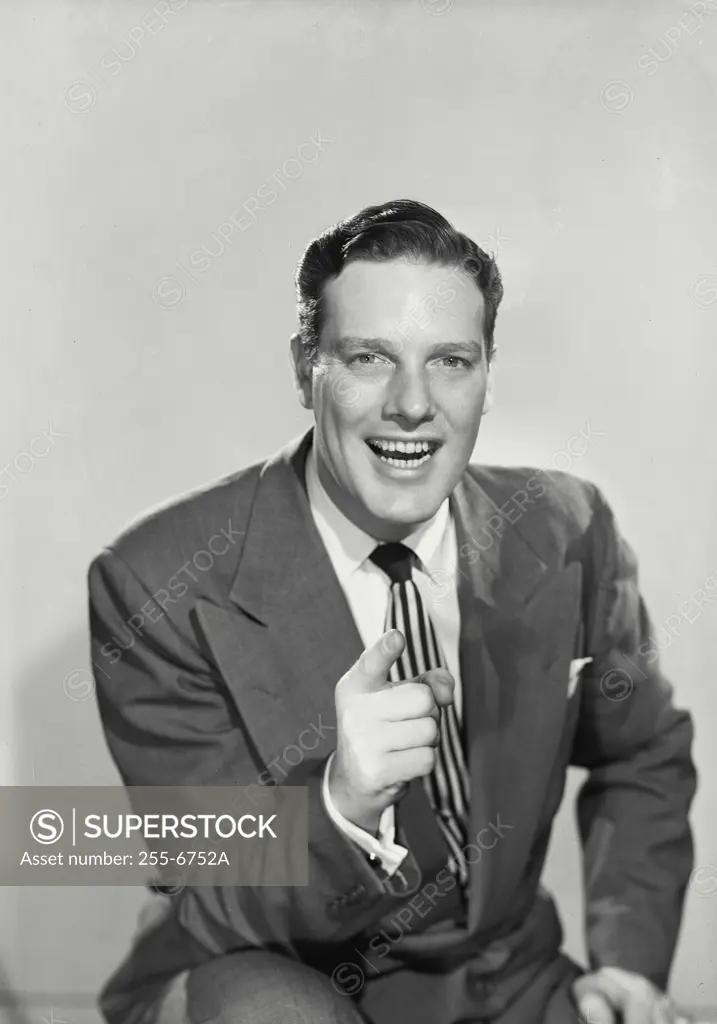 Vintage Photograph. Smiling dark haired man wearing suit and striped tie pointing index finger at camera